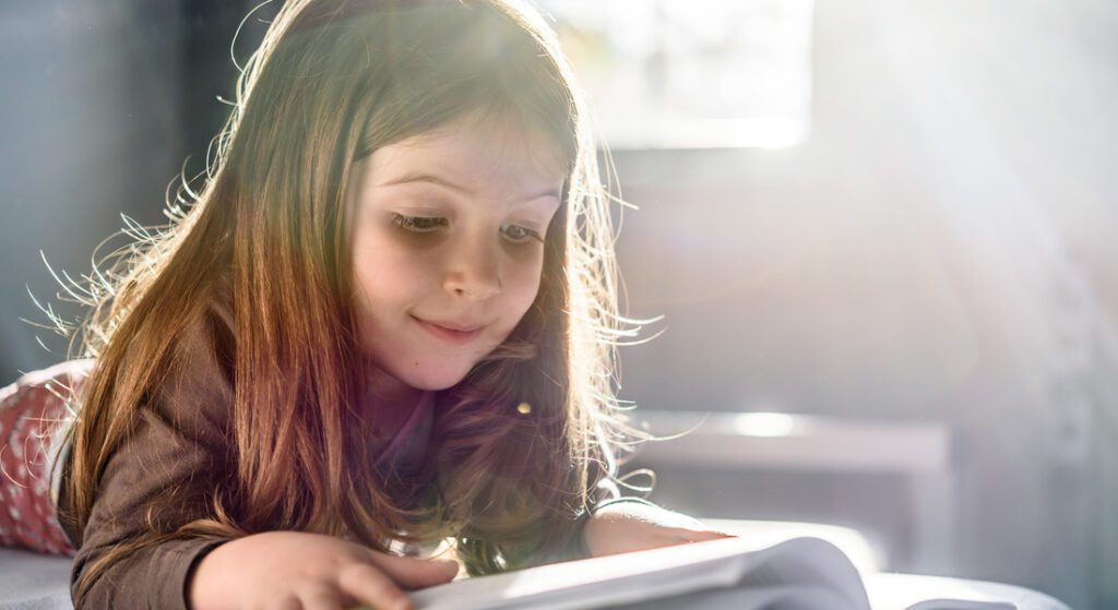 Young girl reading a book while lying on her stomach