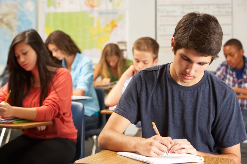 Male Pupil Writing Test At Desk In Classroom