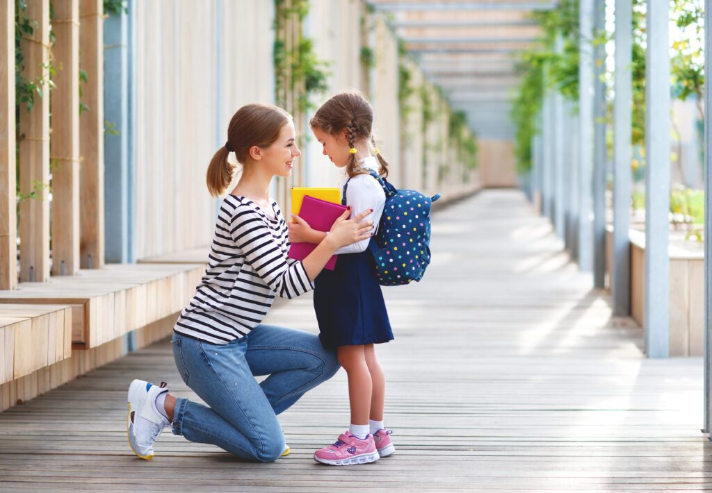 mother crouching in front of daughter in outdoor school corridor