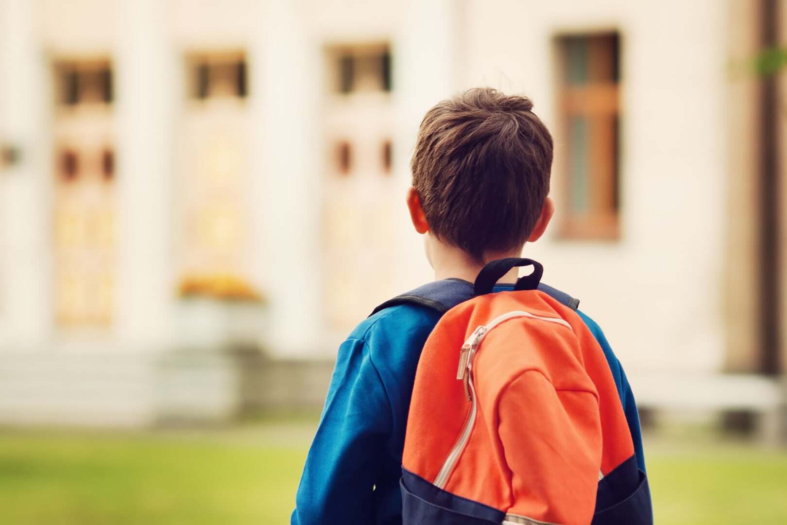 child heading back to school with a back pack with school in the backgound
