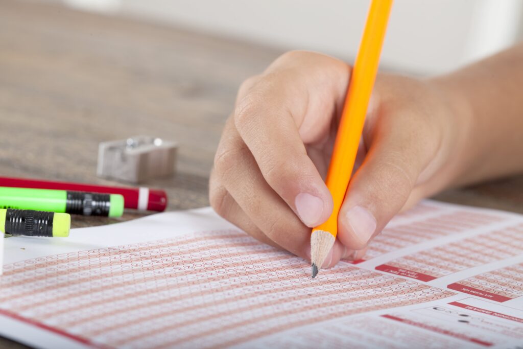 Student's hand filling in answer sheet on desk.