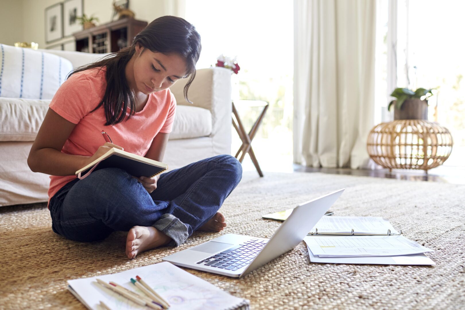 Student sitting on floor with laptop and textbook.